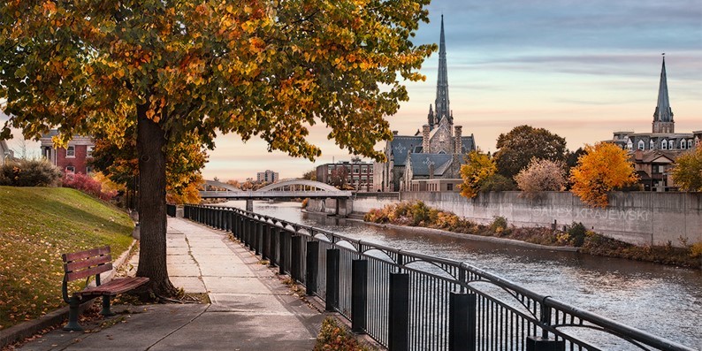 "Fall Bench" is photograph by Alex Krajewski of a Grand River view from the Grand River bank of West Galt, Main Street Bridge and Central Church in Cambridge, Ontario